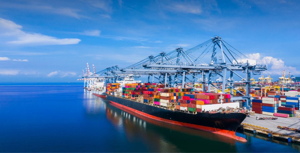 2026년 3월 중동 전쟁으로 인한 해상 운임 급등과 호르무즈 해협 물류 대란 속에서 항구에 적재된 컨테이너와 대형 화물선을 포착한 이미지.