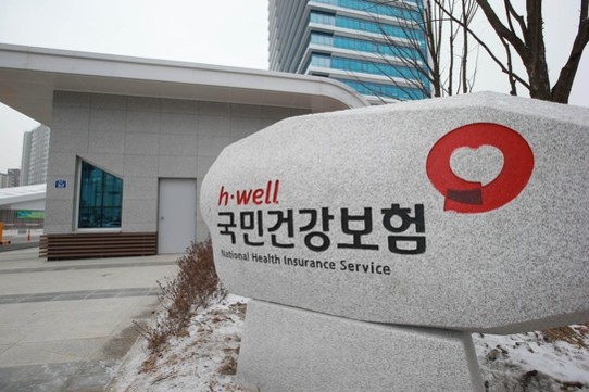 대한민국 국민건강보험공단(NHIS)의 로고와 본부 건물의 현대적인 외관 전경 사진. 공공기관의 신뢰감을 주는 푸른색 계열의 브랜드 색상과 '국민건강보험' 명칭이 명확하게 보이는 이미지.